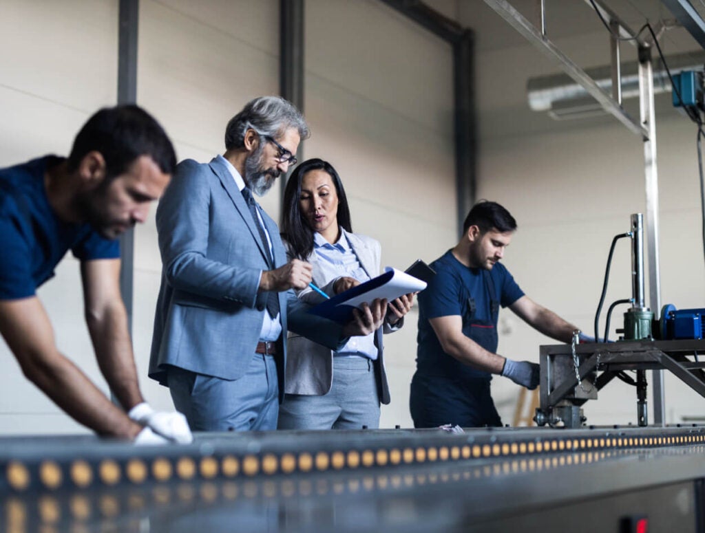 People working on a manufacturing floor, next to an assembly line.